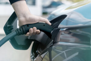 Man Plugging In Charger Into An Electric Car At Charge Station